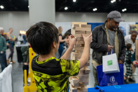 Youth plays giant Jenga at Camp Fire's booth at Best of Alaska showcase 2024.