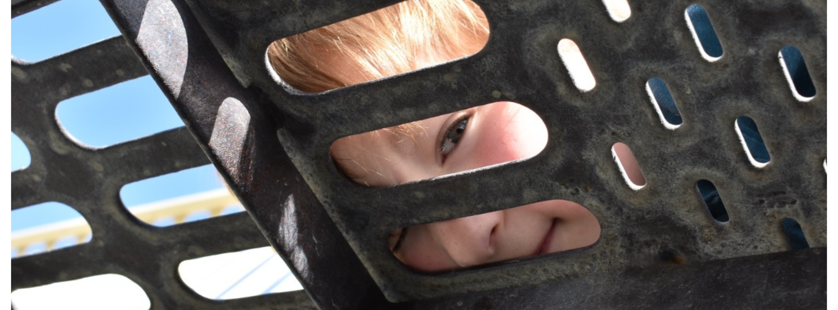 Camp Fire Alaska Blog Image_ Storytelling - a youth looks through the playground grate at the camera