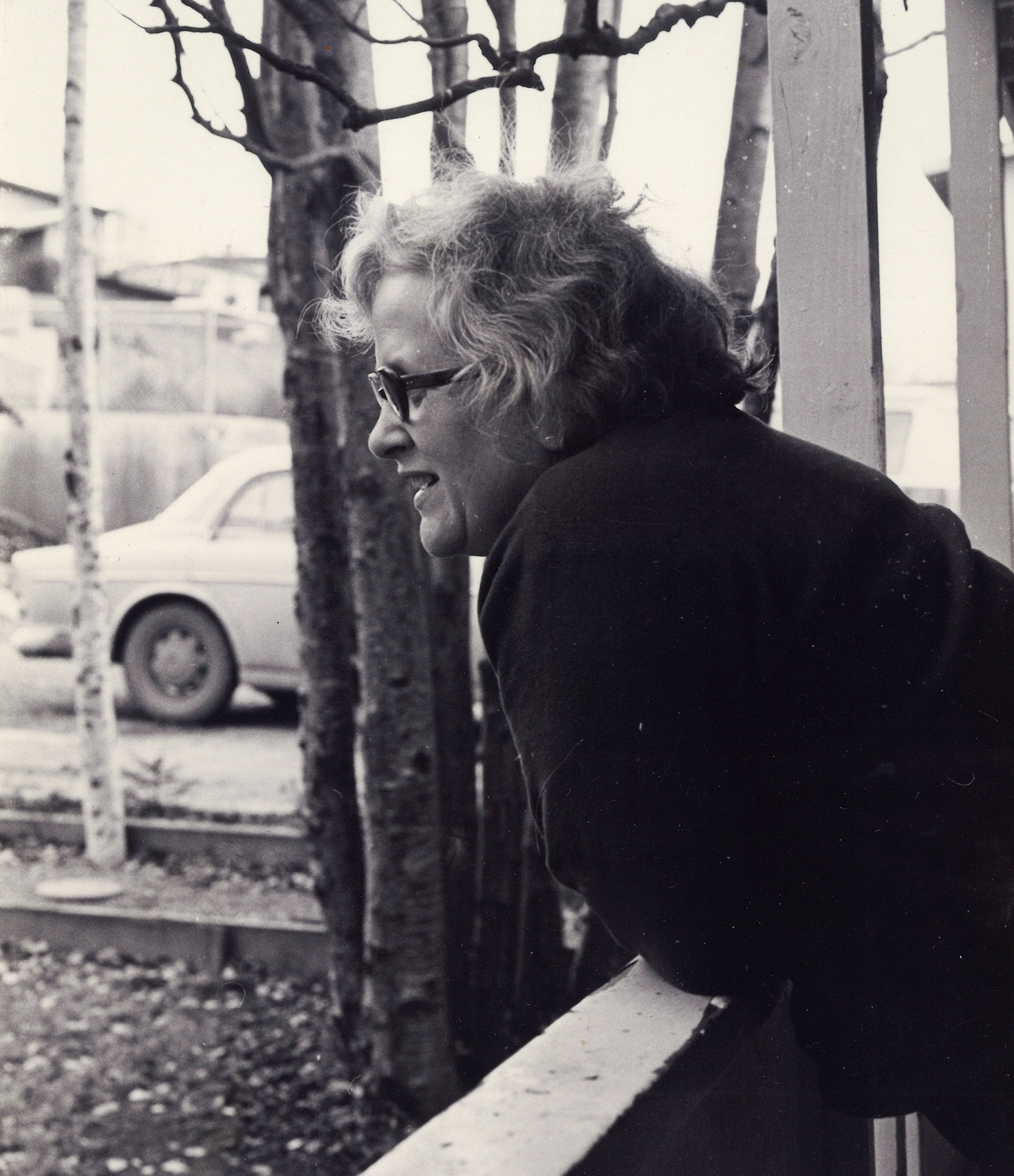 Side profile of a woman leaning on a balcony railing looking out into a yard
