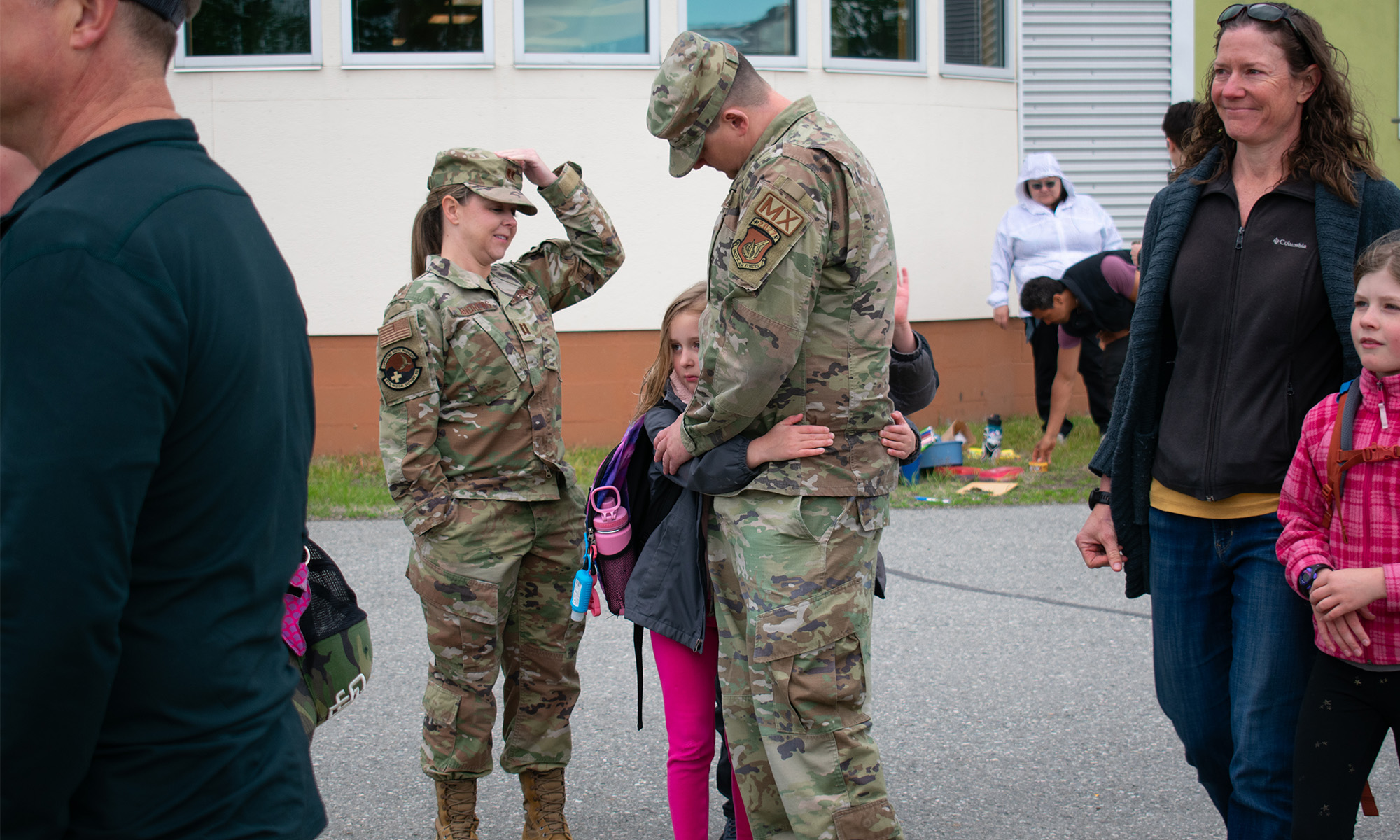 A child hugs a person in a military uniform, while another uniformed person looks down at calmy.